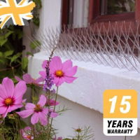 A row of Defender wide plastic pigeon spikes installed on a white window ledge with pink flowers in the foreground, highlighting the 15-year warranty badge.